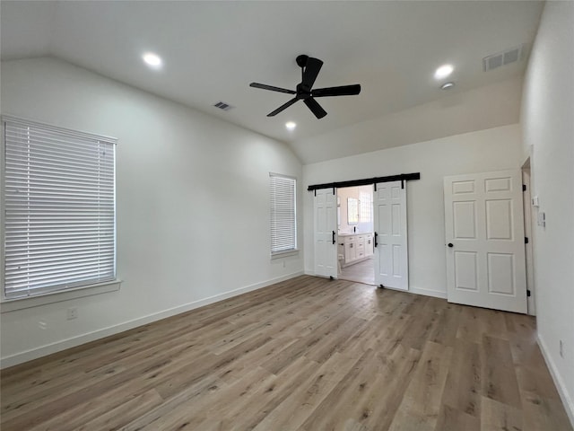 spare room with ceiling fan, lofted ceiling, a barn door, and light wood-type flooring