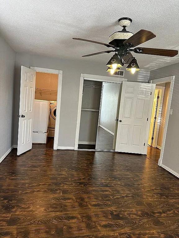 unfurnished bedroom featuring ceiling fan, dark wood-type flooring, a textured ceiling, a closet, and washer and clothes dryer