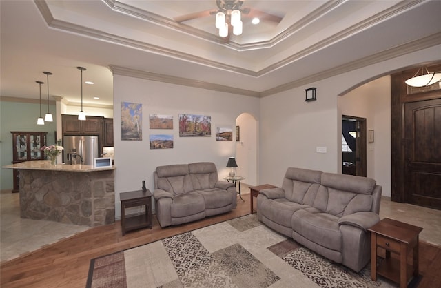 living room with a tray ceiling, crown molding, ceiling fan, and light wood-type flooring