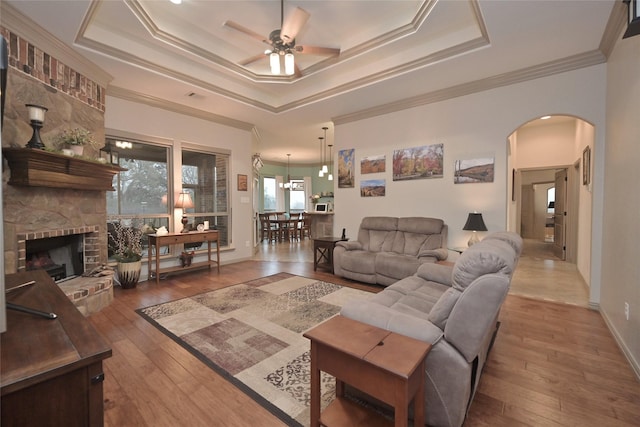 living room featuring a tray ceiling, crown molding, hardwood / wood-style floors, and a brick fireplace