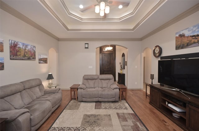 living room with ceiling fan, light wood-type flooring, crown molding, and a tray ceiling