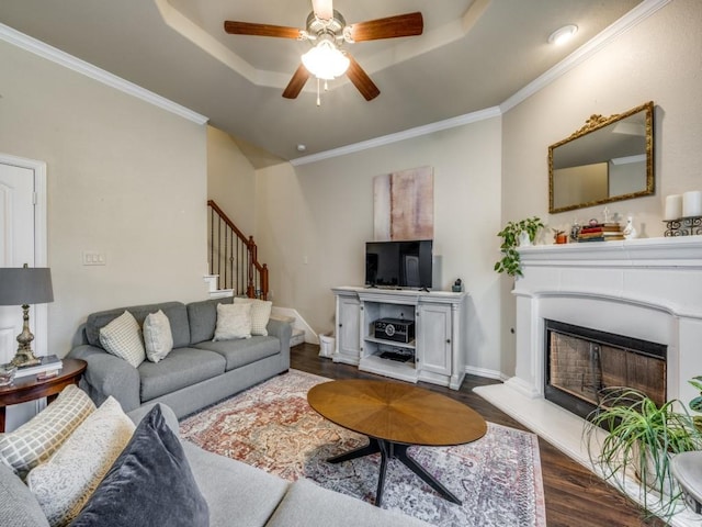 living room with dark hardwood / wood-style floors, ceiling fan, crown molding, and a tray ceiling