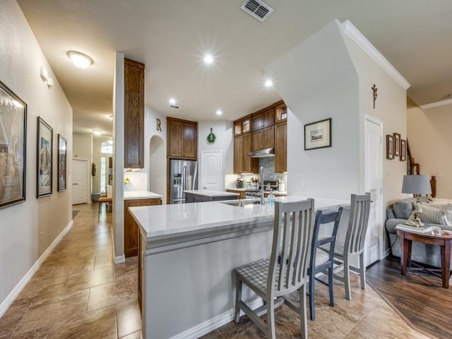 kitchen with sink, kitchen peninsula, a breakfast bar area, appliances with stainless steel finishes, and ornamental molding