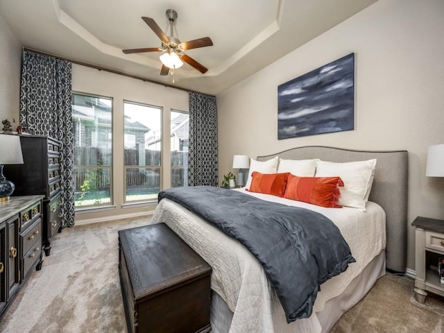 carpeted bedroom with a raised ceiling and ceiling fan