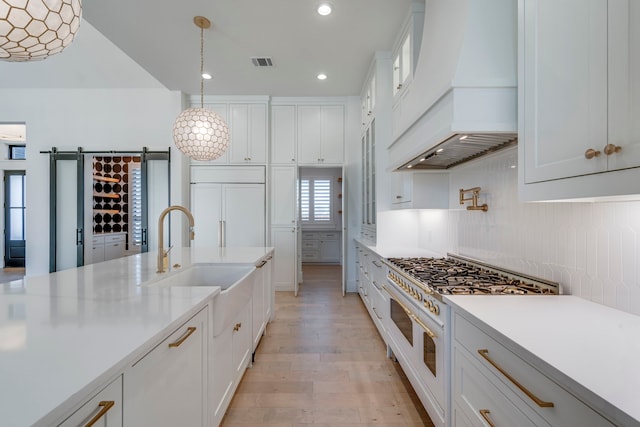 kitchen with custom exhaust hood, white cabinetry, premium appliances, pendant lighting, and a barn door