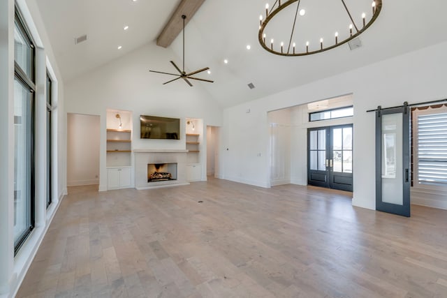 unfurnished living room with light hardwood / wood-style flooring, beam ceiling, high vaulted ceiling, french doors, and a barn door