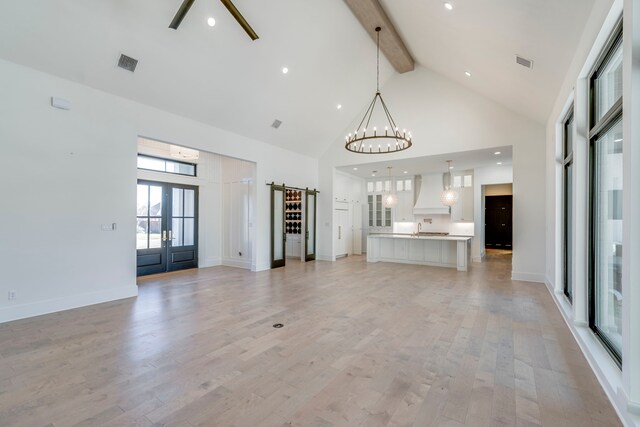 unfurnished living room featuring beam ceiling, a chandelier, high vaulted ceiling, and light hardwood / wood-style flooring