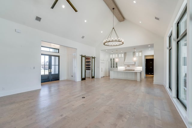 unfurnished living room featuring high vaulted ceiling, beam ceiling, light hardwood / wood-style floors, a barn door, and an inviting chandelier