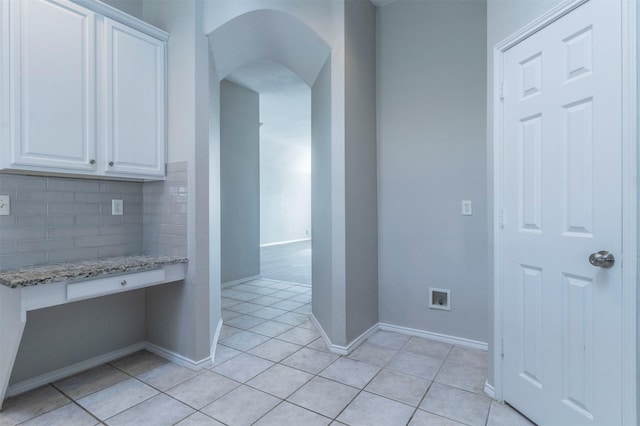 kitchen featuring backsplash, light stone countertops, light tile patterned floors, and white cabinets