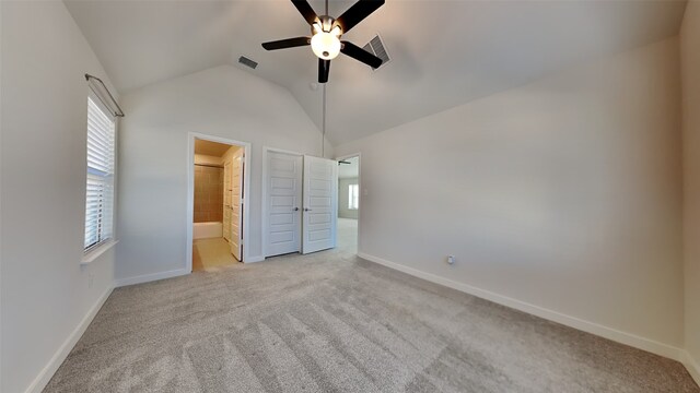 unfurnished bedroom featuring multiple windows, connected bathroom, vaulted ceiling, and light carpet