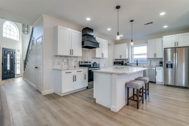 kitchen with a center island, light hardwood / wood-style flooring, white cabinets, custom range hood, and appliances with stainless steel finishes