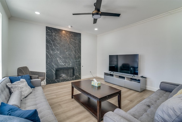 living room featuring ornamental molding, ceiling fan, a fireplace, and light wood-type flooring