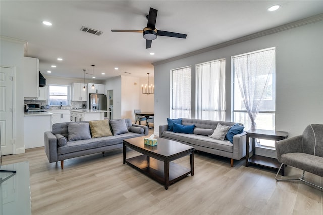 living room featuring sink, ceiling fan with notable chandelier, ornamental molding, and light wood-type flooring