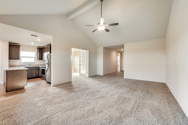 unfurnished living room with beam ceiling, ceiling fan, sink, high vaulted ceiling, and light carpet