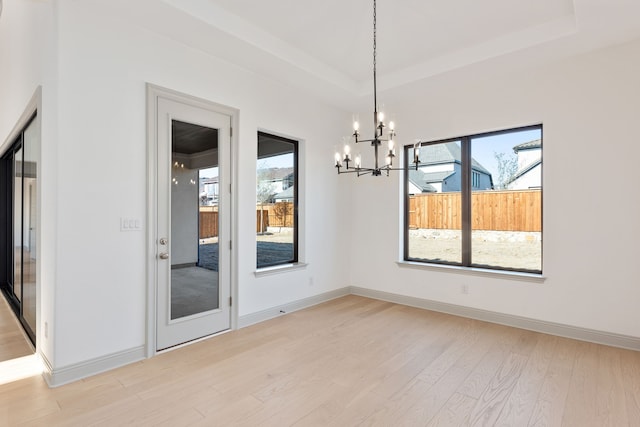 unfurnished dining area featuring an inviting chandelier, a healthy amount of sunlight, a raised ceiling, and light hardwood / wood-style flooring