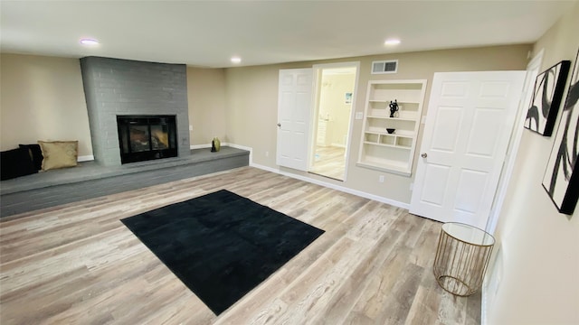 living room featuring light wood-type flooring, built in features, and a brick fireplace