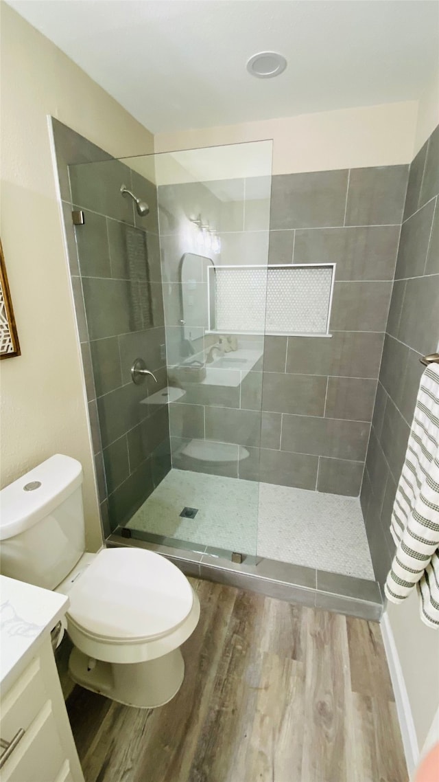 bathroom with toilet, a tile shower, wood-type flooring, and vanity