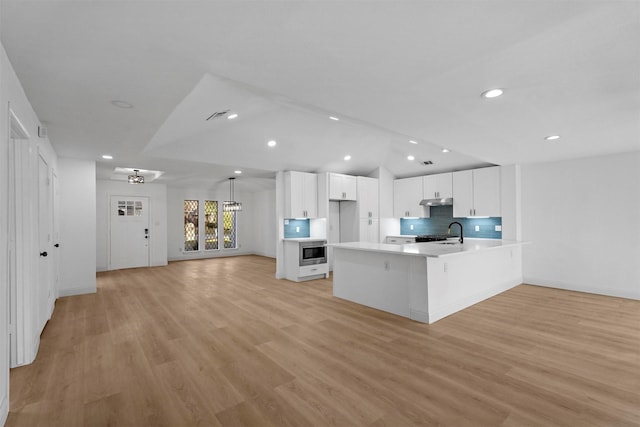 kitchen with light wood-type flooring, tasteful backsplash, built in microwave, sink, and white cabinets