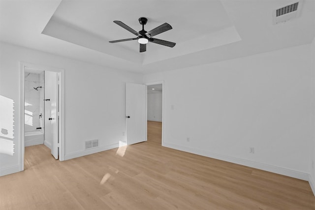 unfurnished bedroom featuring ensuite bathroom, ceiling fan, light hardwood / wood-style flooring, and a tray ceiling