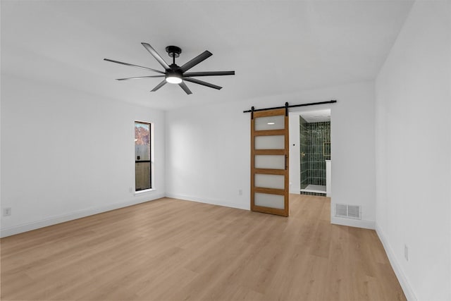 spare room featuring a barn door, light hardwood / wood-style floors, and ceiling fan