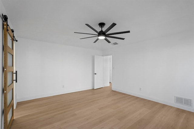 unfurnished room featuring a barn door, light hardwood / wood-style floors, and ceiling fan