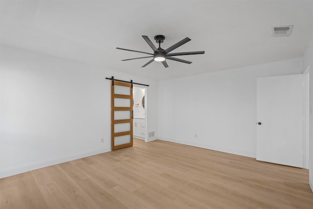 spare room featuring ceiling fan, a barn door, and light wood-type flooring