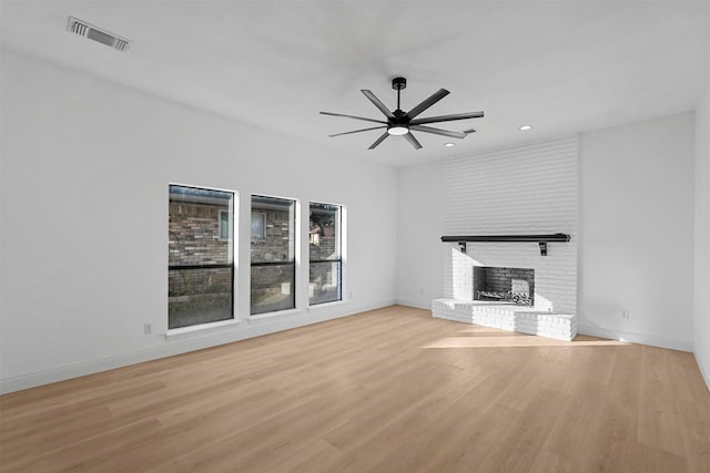 unfurnished living room featuring light wood-type flooring, a brick fireplace, and ceiling fan