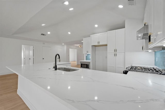 kitchen with white cabinetry, sink, light stone counters, light hardwood / wood-style flooring, and ventilation hood