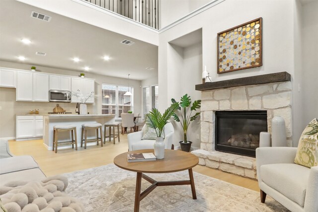 living room featuring a high ceiling, light wood-type flooring, and a stone fireplace