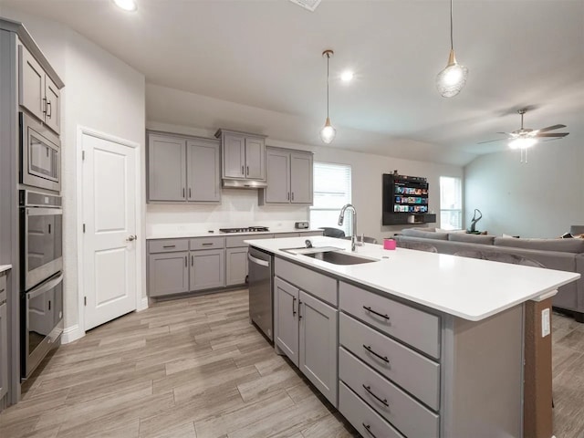 kitchen featuring gray cabinetry, sink, stainless steel appliances, an island with sink, and decorative light fixtures