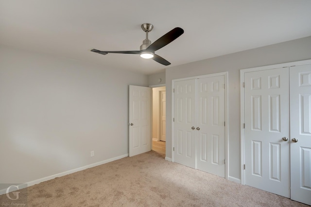 unfurnished bedroom featuring ceiling fan, light colored carpet, and two closets