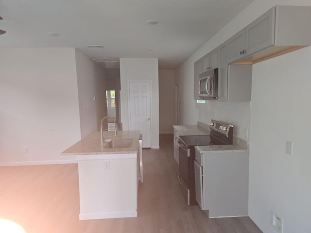 kitchen featuring a center island with sink, sink, light hardwood / wood-style flooring, electric range, and decorative backsplash