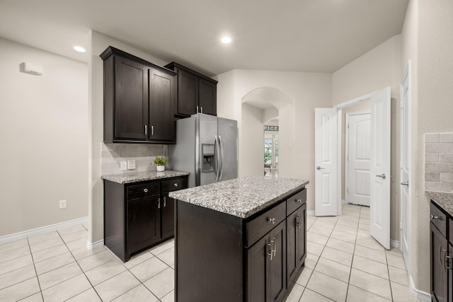 kitchen with dark brown cabinetry, tasteful backsplash, a center island, light tile patterned floors, and stainless steel fridge