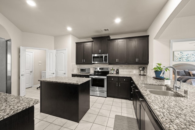 kitchen with light stone countertops, appliances with stainless steel finishes, backsplash, sink, and a center island