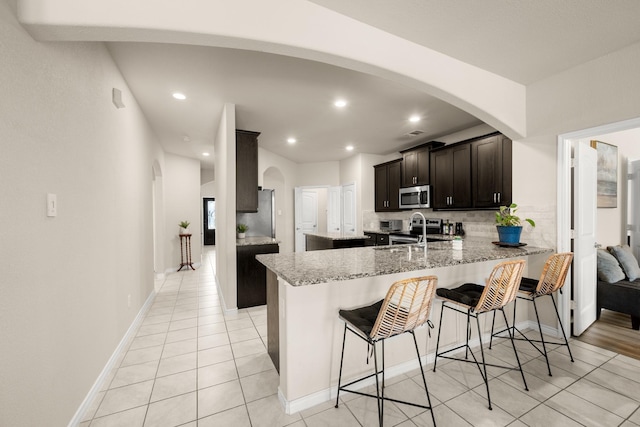 kitchen featuring kitchen peninsula, a kitchen breakfast bar, decorative backsplash, light stone counters, and sink