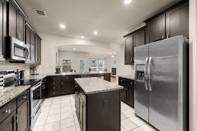 kitchen with a center island, stainless steel appliances, tasteful backsplash, kitchen peninsula, and light tile patterned flooring