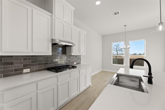 kitchen with white cabinetry, sink, hanging light fixtures, gas stovetop, and a notable chandelier