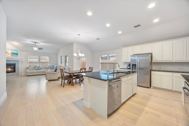 kitchen with stainless steel appliances, vaulted ceiling, sink, an island with sink, and a tiled fireplace