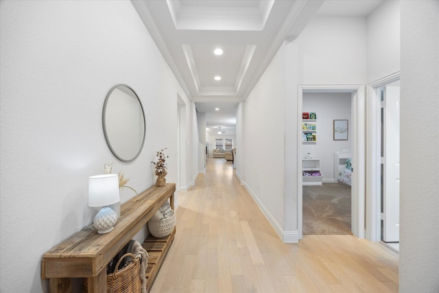 hallway featuring a tray ceiling, crown molding, and light wood-type flooring