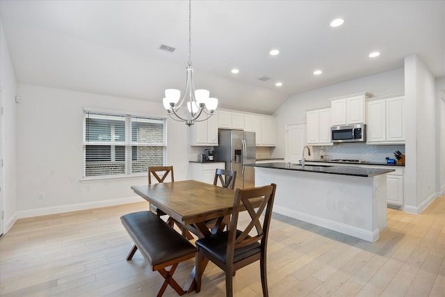 dining area featuring light hardwood / wood-style flooring, a notable chandelier, lofted ceiling, and sink