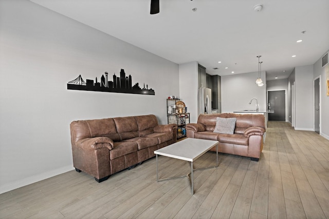 living room with ceiling fan, sink, and light wood-type flooring