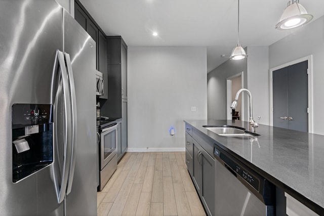 kitchen with appliances with stainless steel finishes, dark stone counters, sink, pendant lighting, and light hardwood / wood-style floors