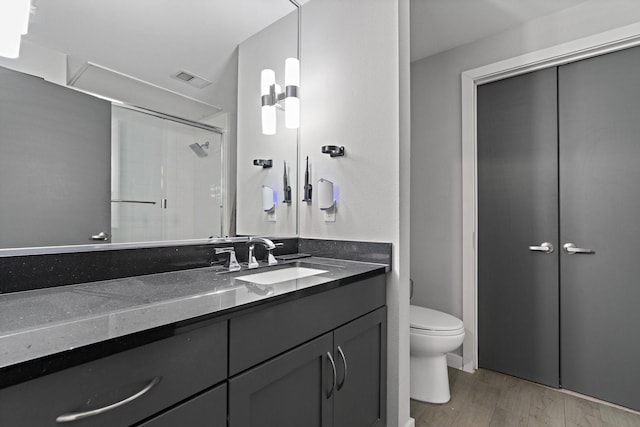 bathroom featuring hardwood / wood-style floors, vanity, a shower with shower door, and toilet