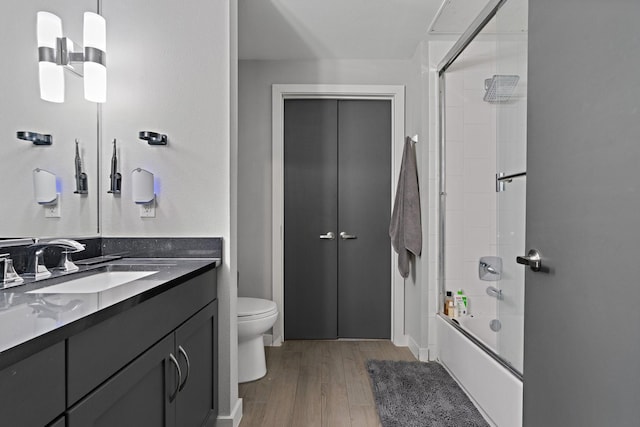 full bathroom featuring bath / shower combo with glass door, vanity, wood-type flooring, and toilet