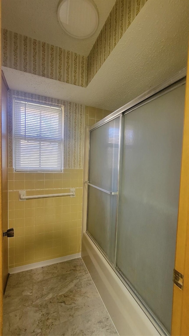 bathroom with shower / bath combination with glass door and tile walls