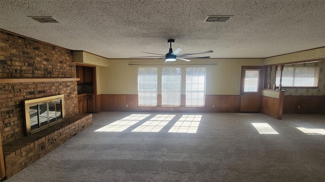 unfurnished living room with a textured ceiling, a brick fireplace, ceiling fan, and wood walls