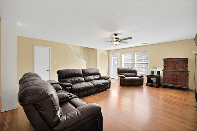 living area with ceiling fan, light wood finished floors, arched walkways, and visible vents