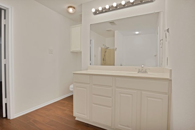 bathroom with toilet, wood finished floors, vanity, baseboards, and walk in shower