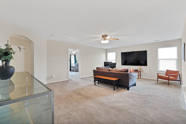 living room with arched walkways, light colored carpet, a ceiling fan, baseboards, and attic access