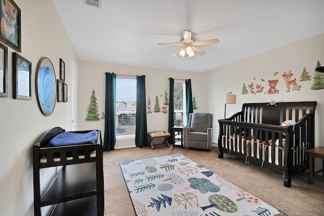 bedroom featuring light carpet, visible vents, a crib, and a ceiling fan